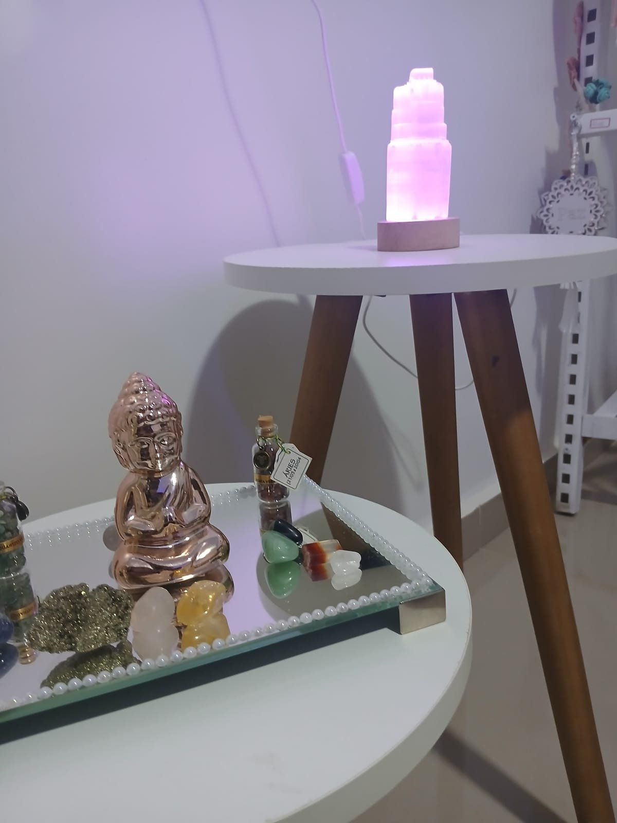 Luminária de pedra acesa em rosa sobre a mesinha, com um Buda e cristais sobre o espelho