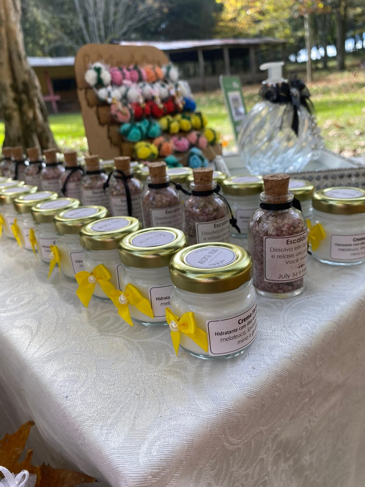 Vidrinhos de sal de escalda-pés com rolha e potes de creme hidratante de tampa dourada, na mesa do ateliê
