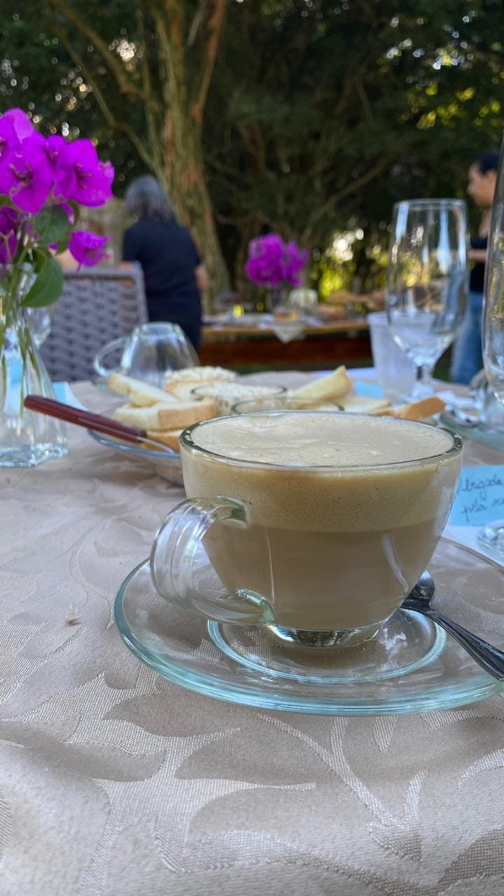Xícara de vidro com café com leite na mesa ao ar livre, com buganvílias ao fundo