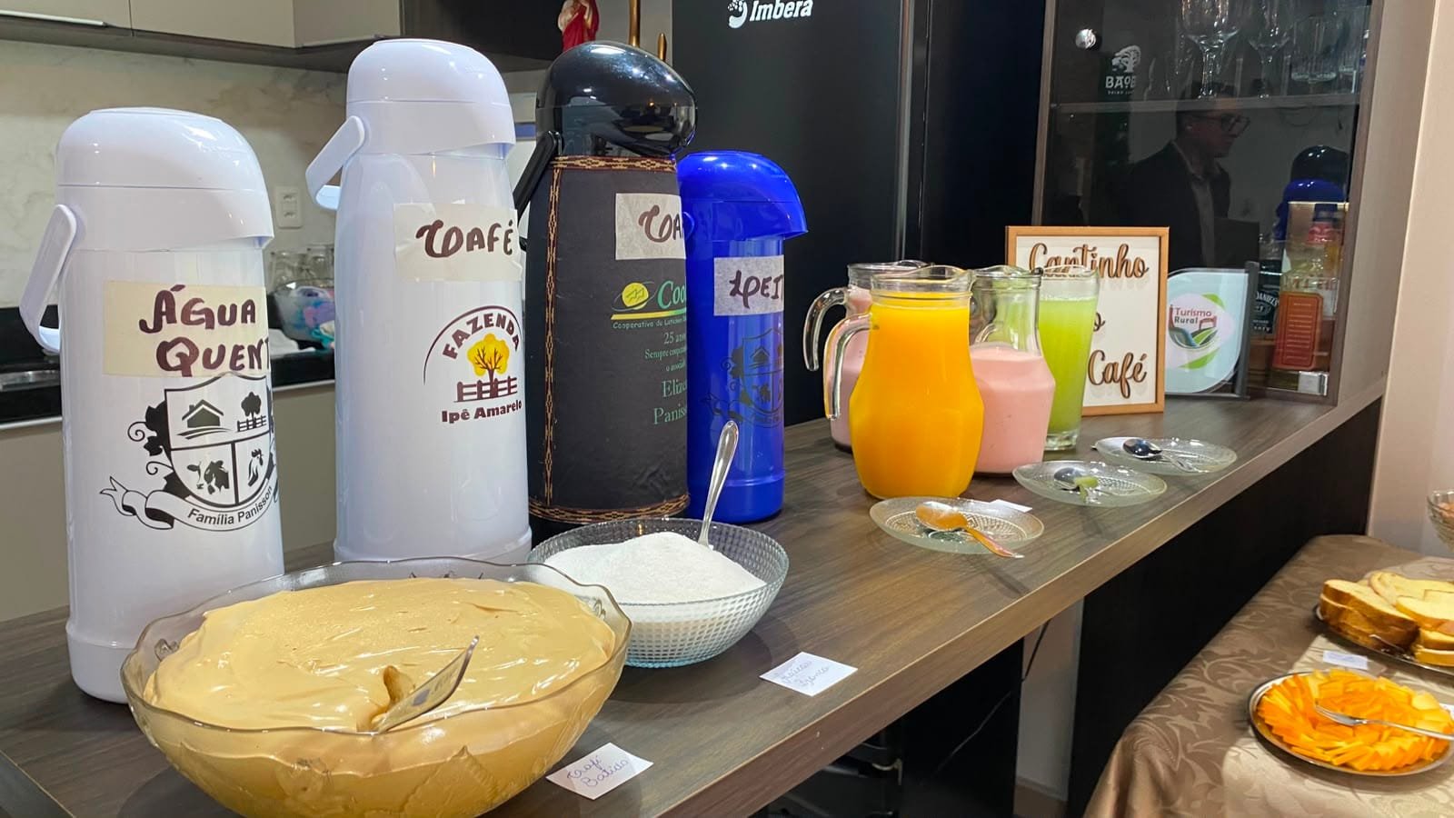Garrafas térmicas de café e de água quente, jarras de suco e uma tigela de creme no balcão