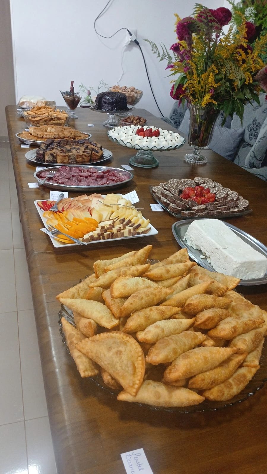 Travessa de pastéis fritos na frente de uma mesa de frios, queijos e doces