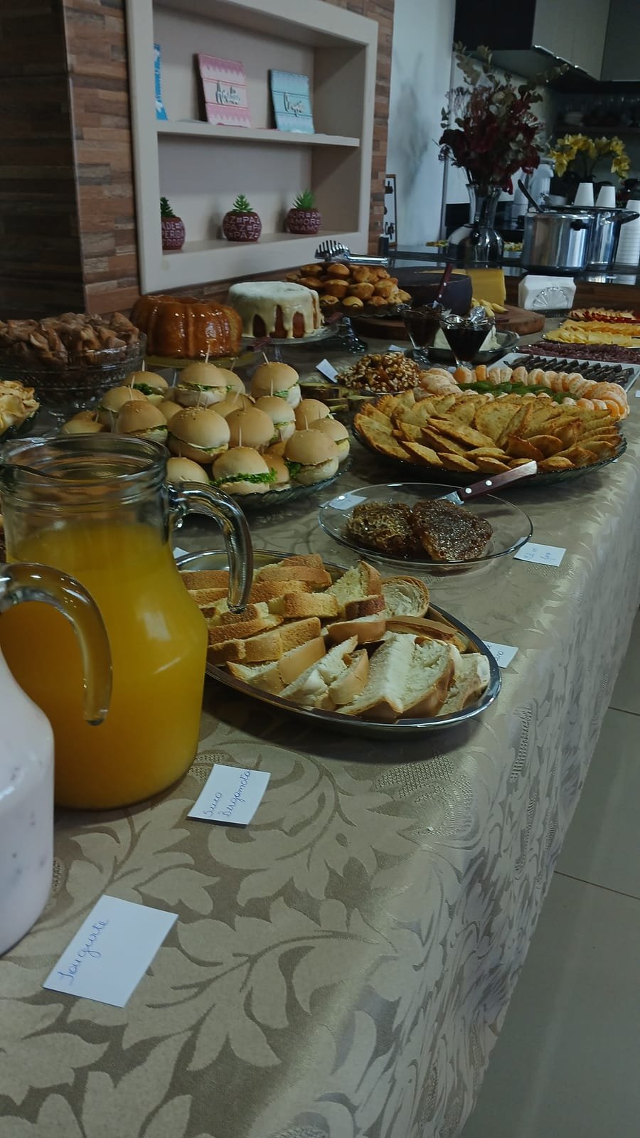 Mesa comprida com pães, salgados, doces e uma jarra de suco de laranja