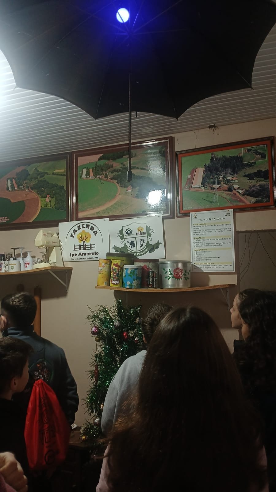 Pinturas da fazenda na parede e prateleiras com latas e objetos antigos, com uma turma de escola na frente