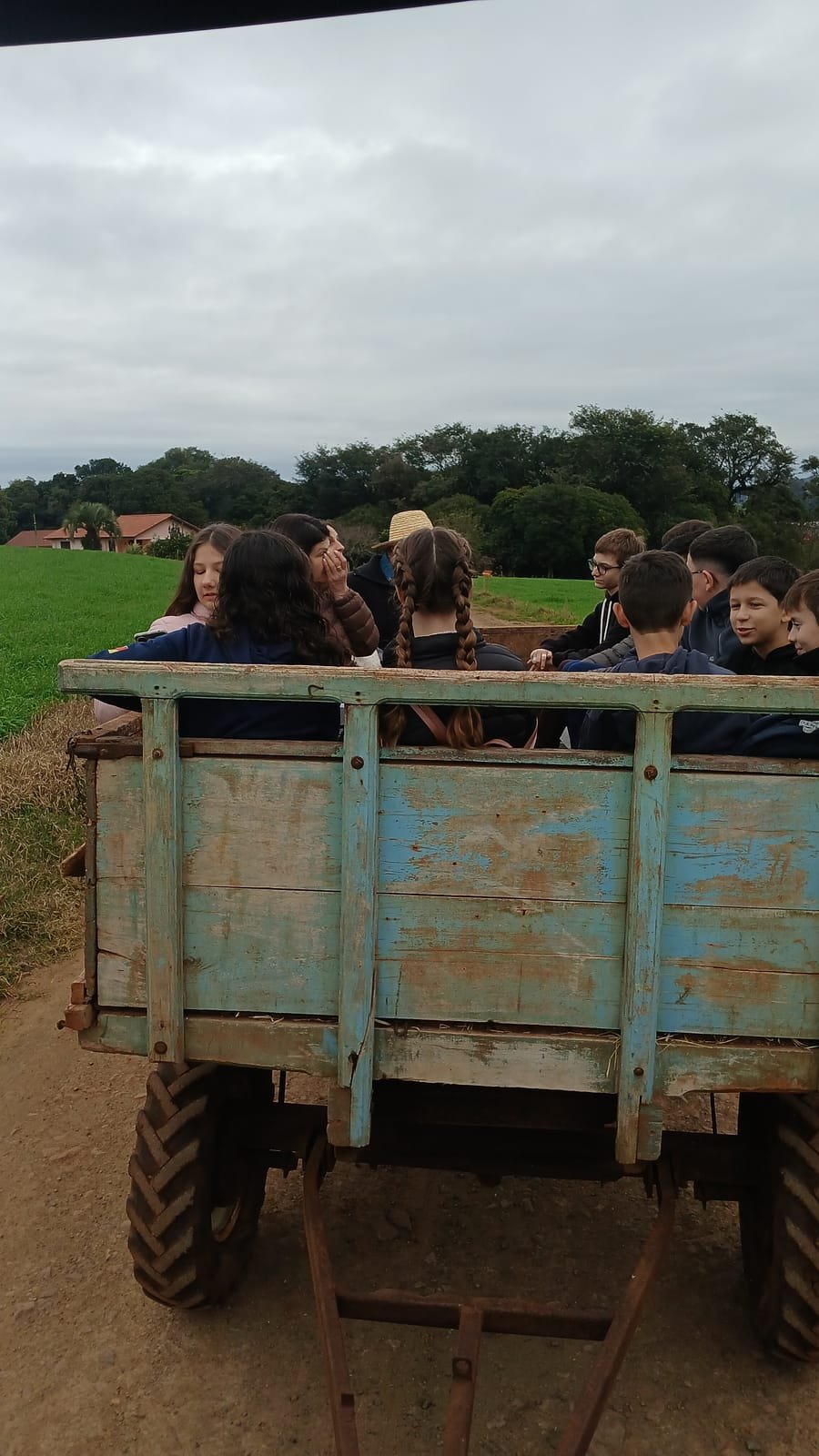 Turma de estudantes sentada no carroção, com a lavoura e as árvores ao fundo