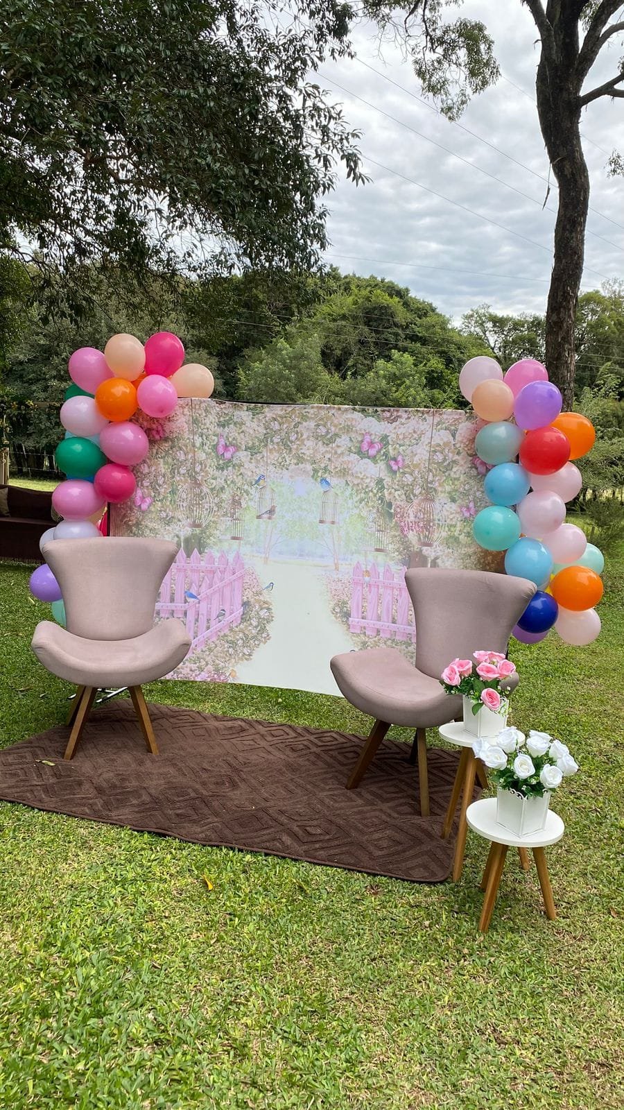 Painel com balões coloridos, duas poltronas e flores, montado no gramado