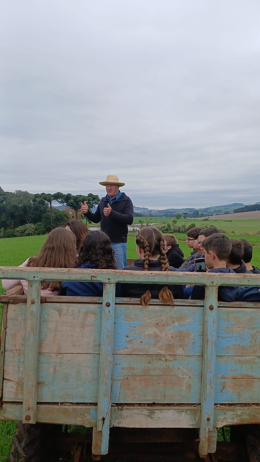 Turma de estudantes no carroção ouvindo o anfitrião, no meio das lavouras