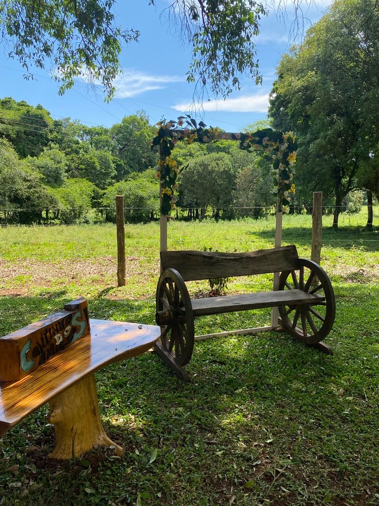 Banco de madeira à sombra, com o campo aberto na frente